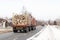 A truck with a trailer carries logs along a snow-covered asphalt road. Removal of wood for processing. Industrial winter logging