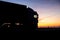 A truck with a trailer rides on the motorway at night against the backdrop of an orange sunny sunset. The concept of the