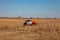 A truck for the transportation of gasoline and fuel with an orange tank rides in a yellow field on the road during the delivery of