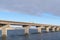 Truck travelling on a beam bridge over lake against rugged land and cloudy sky