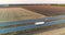 Trucks drive along the highway among the fields at sunset. Trucks travel on a straight road at sunset top view