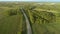 Trucks ride along the highway among trees and green fields. Aerial view. Cargo delivery on an asphalt road. Asphalt road