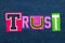 TRUST text word collage in brightly colored fabric on blue denim, confidence and fidelity