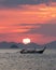 Tthai longtail boat in the sea at sunset with big red sun and mountains silhouettes and clouds