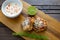 TTwo shrimp cakes on a cutting board with a lemon garlic dipping sauces lemon wedge and a stem or rosemary on a wooden table..