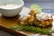 TTwo shrimp cakes on a cutting board with a lemon garlic dipping sauces lemon wedge and a stem or rosemary on a wooden table..