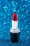 Tube of Classic Bright Red Lipstick on a Blue Glittery Background