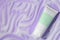 Tube with cleansing foam on violet background, top view. Cosmetic product