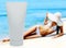 Tube of sun lotion with slim tanned woman on a beach behind.