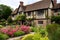 tudor house surrounded by lush gardens, with blooming flowers and shrubs