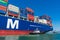 Tugboat assists container ship CMA CGM out of the Port of Oakland under blue sky