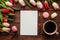 Tulip flowers, empty blank of paper, pen, french macaroons pastries and cup of coffee on a dark wooden background. Holiday mockup