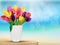 Tulip flowers in rainbow colours in a white glass on the beach