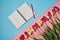 Tulips and open blank notebook on pink and blue pastel background, copy space. Sping minimal concept.