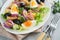 Tuna salad with pasta, eggs, potatoes, olives, red onions and sauce in white plate on old light gray concrete table background