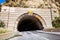 Tunnel carved into a mountain on Highway 1, California; maximum height displayed at the entrance; highway skewing left due to road