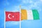 Turkey and Cote d`Ivoire Ivory coast two flags on flagpoles and blue cloudy sky