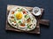 Turkish breakfast - flatbread with fried egg, yogurt, chili sauce and cheese on wooden chopping board, on dark background