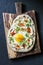 Turkish breakfast - flatbread with fried egg, yogurt, chili sauce and cheese on wooden chopping board, on dark background