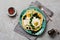 Turkish eggs flatbread with yoghurt, cheese, olives, spinach and red pepper on ceramic vintage plate on gray old background.