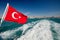 Turkish flag on a boat Ð¸ Ships wake. The ship is leaving the big city.