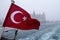 Turkish flag on a ship during a snowstorm, a Europe-Asia ferryboat can be seen in background, as well as the Haydarpasa station