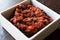 Turkish Meze Acili Ezme or acuka made with fresh tomatoes and spices in square ceramic bowl.