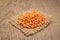 Turkish Red Lentil legume. Grains on square cutout of jute. Wood