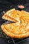 Turkish Tepsi Boregi, Round Borek cheese pie on kitchen board. Black background. Top view