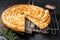 Turkish Tepsi Boregi, Round Borek cheese pie on kitchen board. Black background. Top view