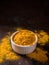 Turmeric powder. Traditional indian golden healthy spice in white ceramic bowl on dark background