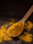 Turmeric powder. Traditional indian golden healthy spice in wooden spoon on dark background