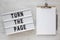 `Turn the page` words on a lightbox, clipboard with blank sheet of paper on a white wooden background, top view. Overhead, from