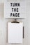 `Turn the page` words on a lightbox, clipboard with blank sheet of paper on a white wooden surface, top view. Overhead, from abo