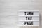 `Turn the page` words on a lightbox on a white wooden surface, top view. Overhead, from above, flat lay. Space for text