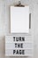 `Turn the page` words on a modern board, clipboard with blank sheet of paper on a white wooden surface, top view. Overhead, from