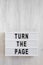`Turn the page` words on a modern board on a white wooden surface, top view. Overhead, from above, flat lay. Copy space