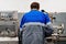 Turner stands behind lathe in production hall and works. View of worker from behind from back in overalls.