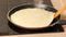 Turning a pancake in a pan. Big round pancake on induction frying pan. Cooking smoke goes up from pancake.