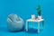 Turquoise armchair bean bag and white coffee table with green flower in a pot, three candles and photo frame on it. Blue