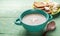 Turquoise ceramic bowl with mushroom cream soup, wooden spoon, garlic, bread, on green wooden background