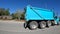 Turquoise colored dump truck passes in slow motion on a clear blue sky day