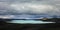 Turquoise colored lake in black ash desert on Iceland beneath stormy sky