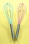 Turquoise and pink kitchen whisks on yellow background