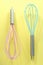 Turquoise and pink kitchen whisks on yellow background