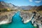 Turquoise river in deep rocky gorge surrounded by high mountains under blue sky on sunny autumn day. Amazing natural landscapes