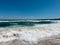 Turquoise sea water with foaming white waves crashing to the shore at sandy beach