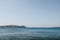 Turquoise sea waters off the coast of Mykonos, Greece, land and a yacht in the distance