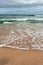 Turquoise sea with waves and sea foam, sandy beach