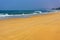 Turquoise sea and yellow sand against blue sky and green hills in the distance. View of long bike traces on the beach on sunny day